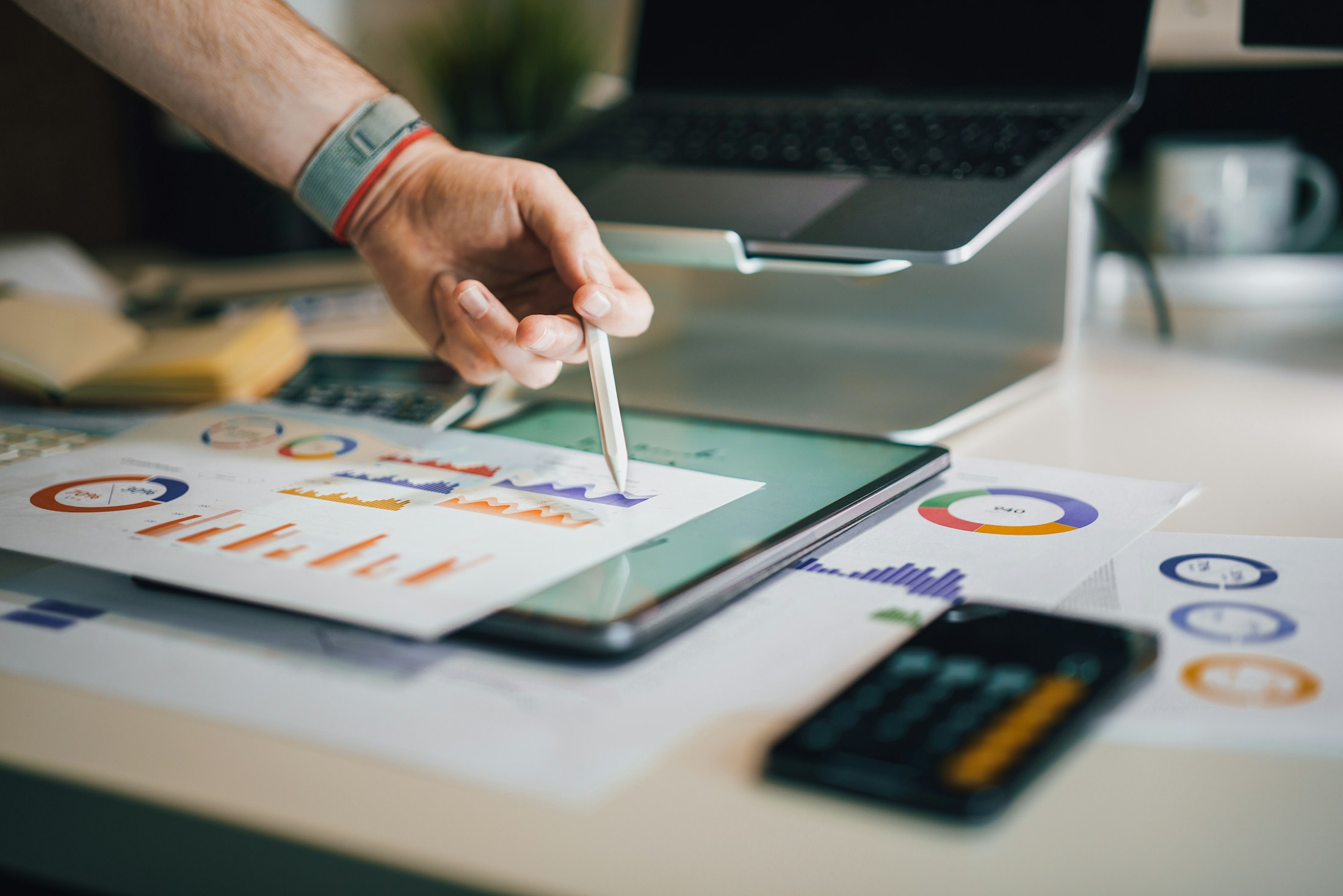 A hand reviewing charts on a tablet beside printed financial analysis
