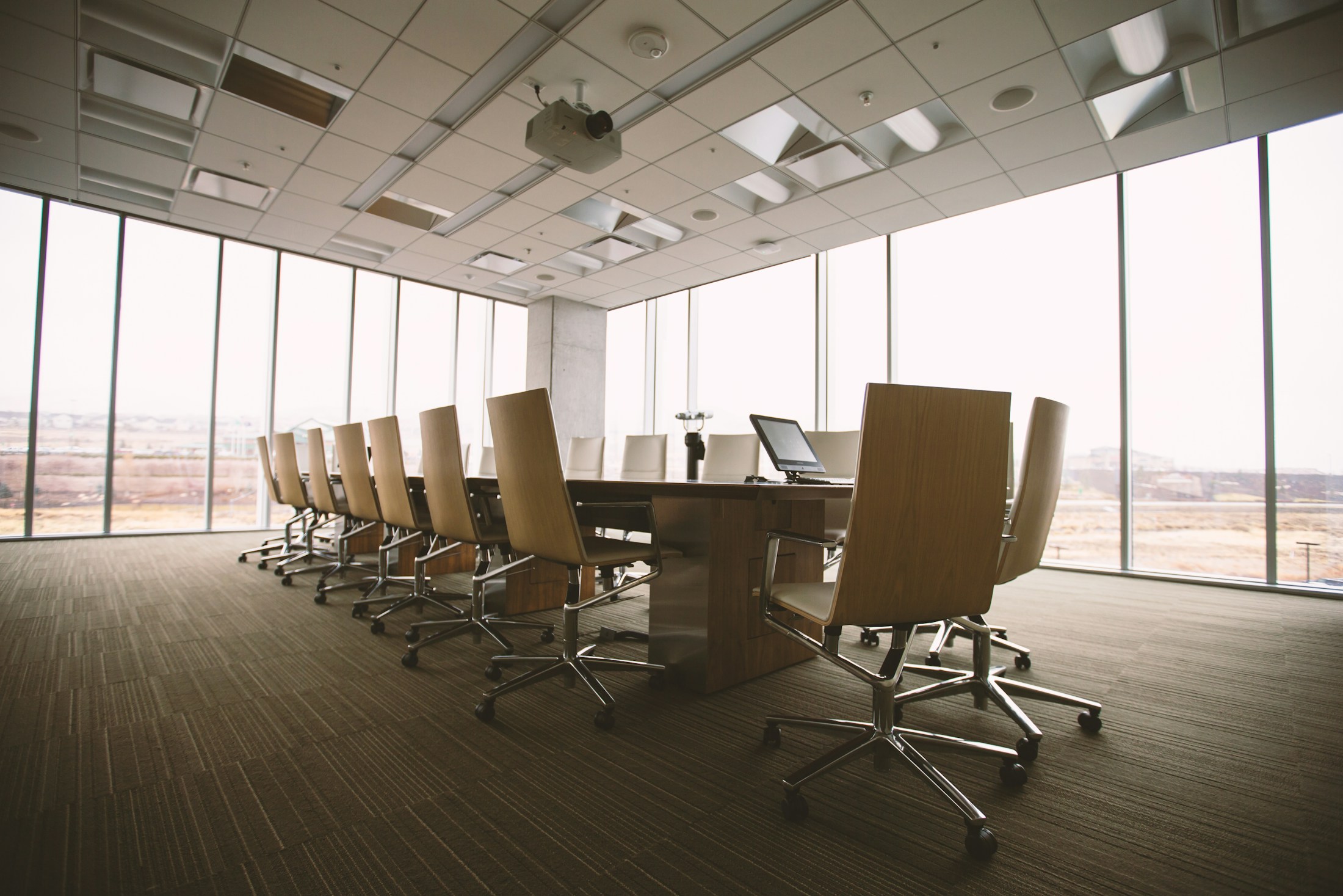 A minimalist boardroom with a wooden table and daylight through glass walls