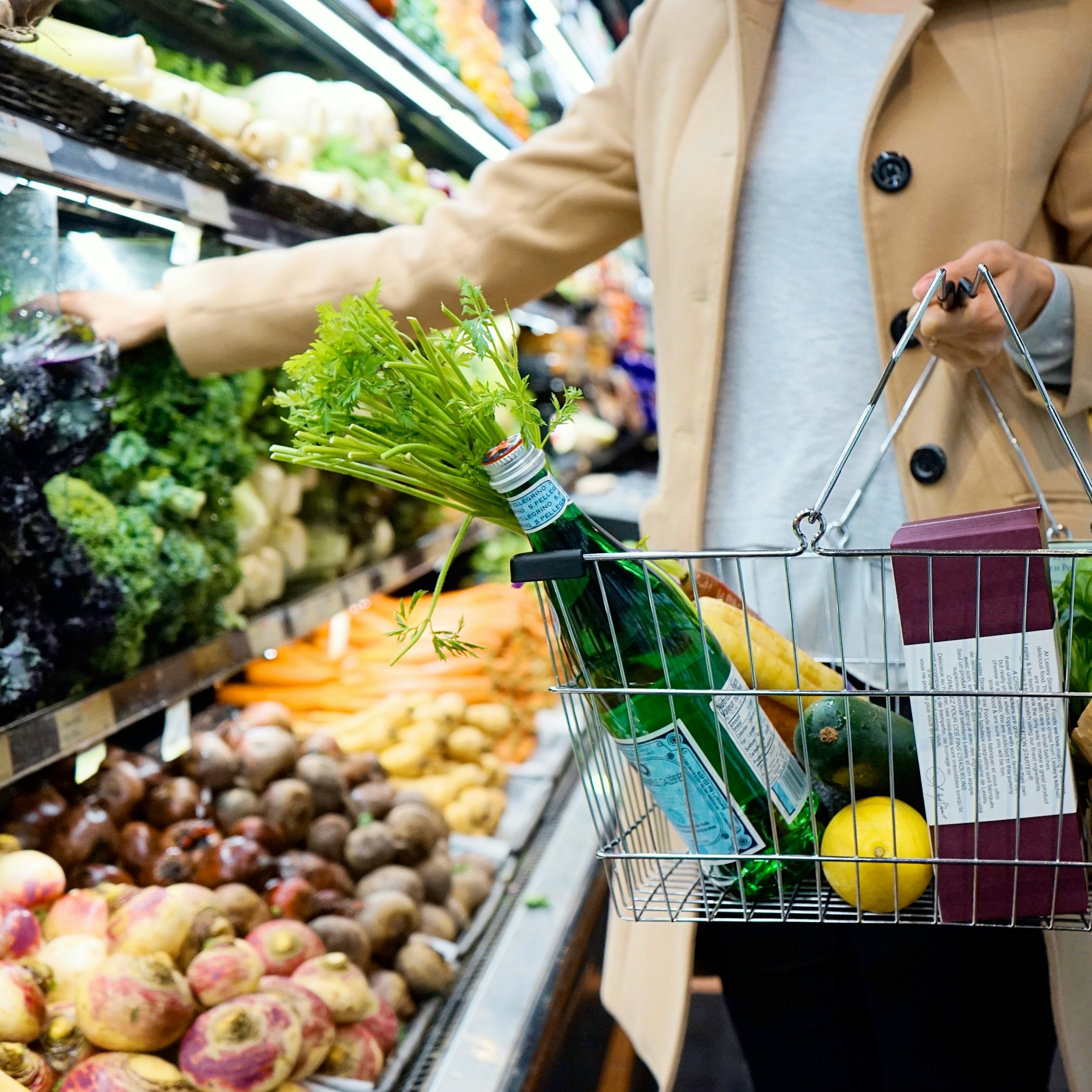 A shopper choosing produce while carrying a basket in a grocery store